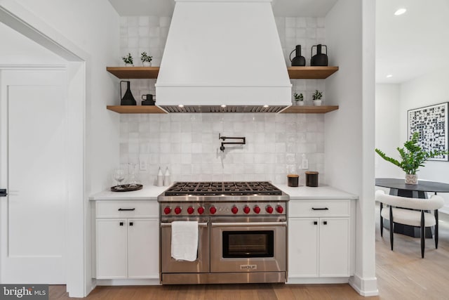 kitchen featuring white cabinets, backsplash, premium range hood, and range with two ovens