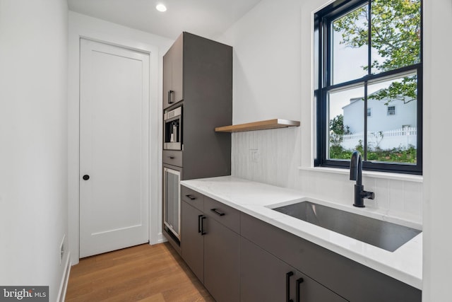 kitchen with light hardwood / wood-style flooring, light stone countertops, sink, and tasteful backsplash