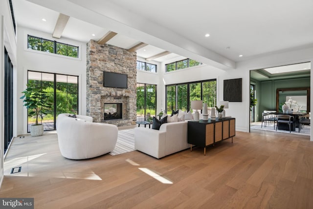 living room featuring a stone fireplace, a wealth of natural light, beamed ceiling, and light wood-type flooring