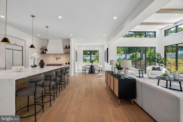 kitchen featuring custom range hood, light wood-type flooring, hanging light fixtures, and white built in refrigerator