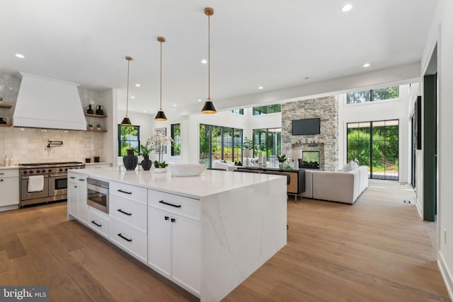 kitchen with built in microwave, a kitchen island, range with two ovens, white cabinets, and custom range hood