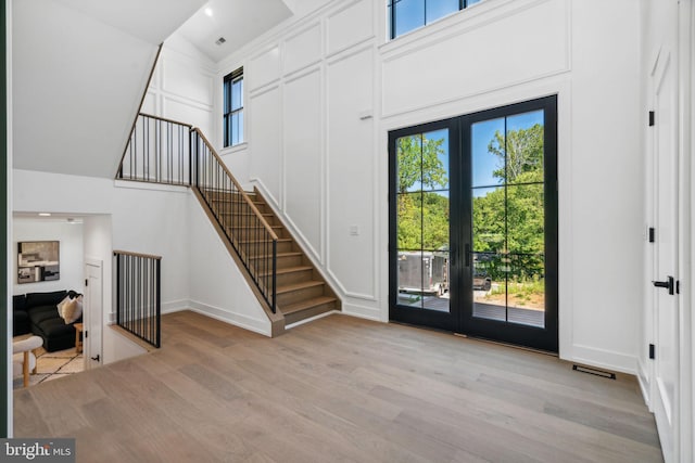 foyer entrance with french doors, light hardwood / wood-style floors, and a high ceiling