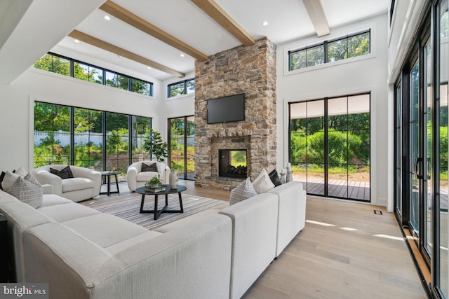 living room featuring beam ceiling, a stone fireplace, light hardwood / wood-style flooring, and a high ceiling