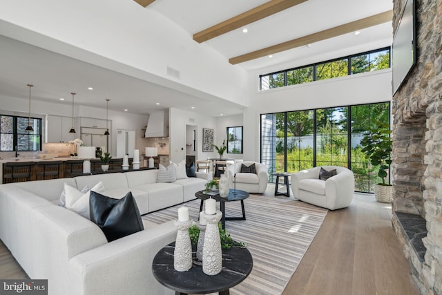 living room featuring beamed ceiling, light wood-type flooring, and a towering ceiling