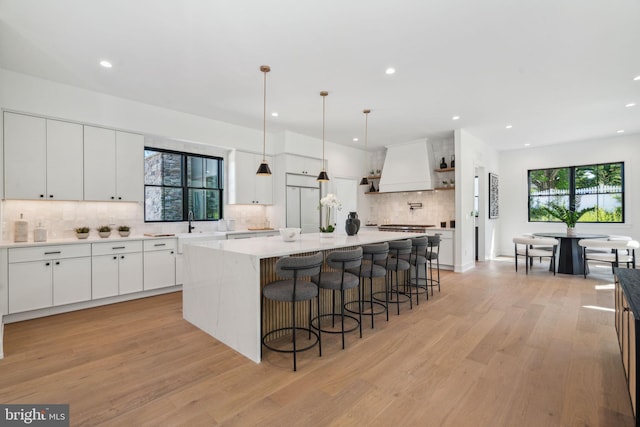 kitchen featuring custom exhaust hood, pendant lighting, light hardwood / wood-style flooring, a center island, and white cabinetry