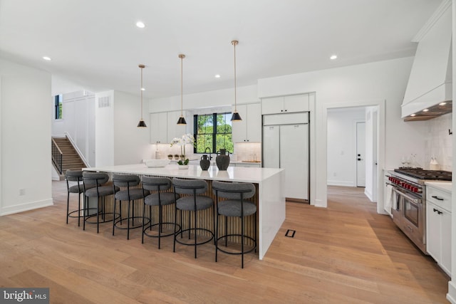 kitchen with white cabinetry, a large island, premium appliances, premium range hood, and decorative light fixtures