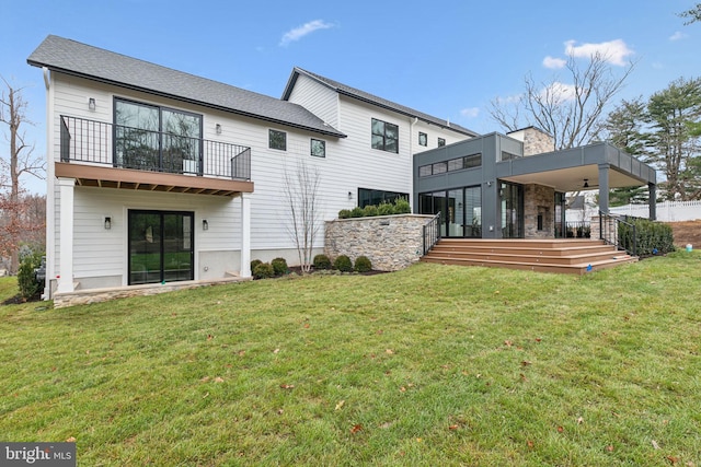 rear view of property featuring ceiling fan, a yard, and a balcony