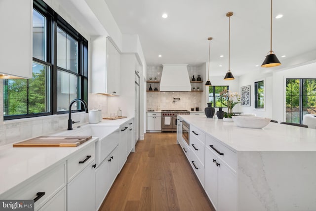 kitchen with white cabinetry, a spacious island, decorative backsplash, custom exhaust hood, and appliances with stainless steel finishes