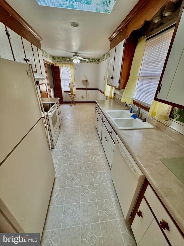 kitchen with a skylight, white appliances, ceiling fan, sink, and white cabinets