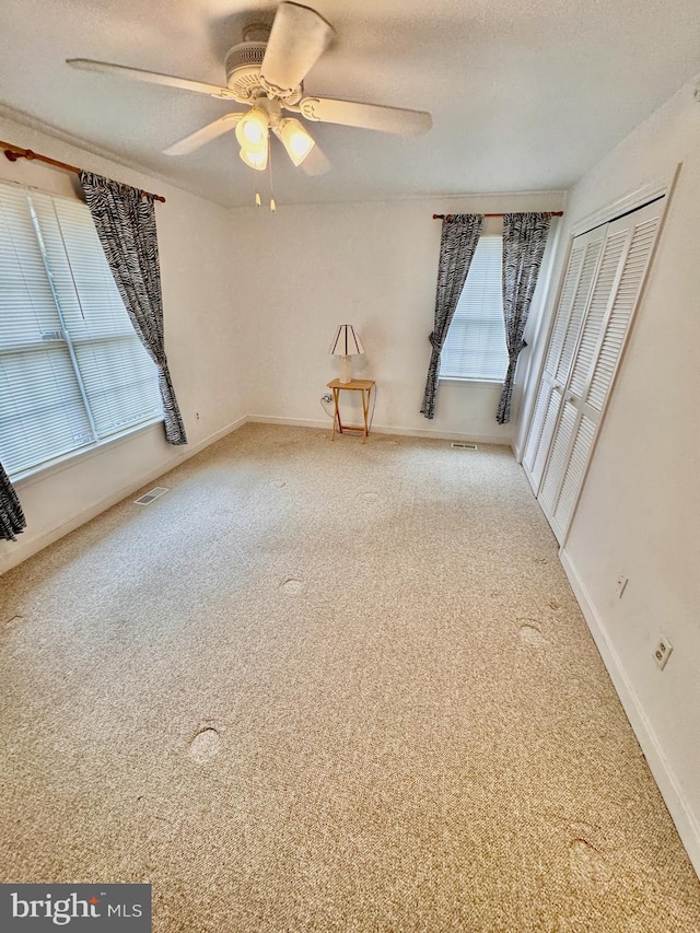 empty room featuring plenty of natural light, ceiling fan, carpet floors, and a textured ceiling