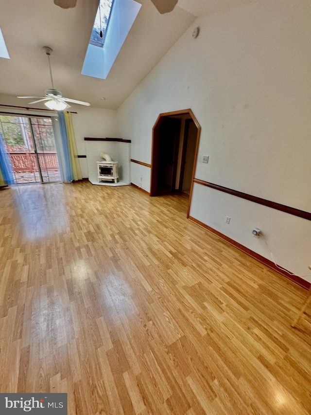 unfurnished living room featuring vaulted ceiling with skylight, ceiling fan, and light hardwood / wood-style floors