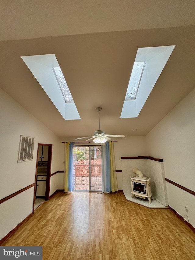 unfurnished living room featuring ceiling fan, light hardwood / wood-style floors, lofted ceiling with skylight, and a wood stove