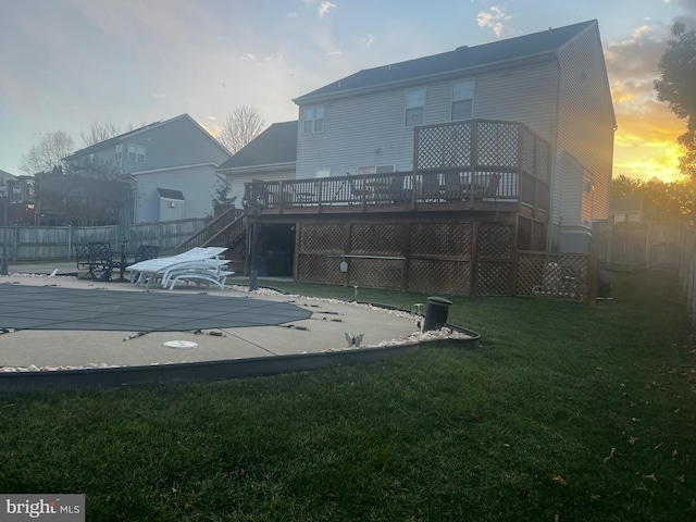 back house at dusk featuring a pool side deck, a patio, and a lawn