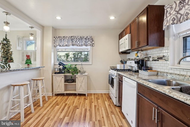 kitchen with light stone countertops, white appliances, sink, light hardwood / wood-style floors, and hanging light fixtures