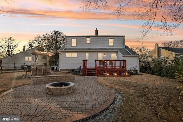 back house at dusk with a wooden deck, a patio area, a yard, and an outdoor fire pit