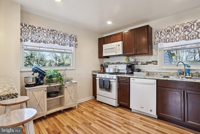 kitchen featuring dark brown cabinetry, light stone countertops, sink, light hardwood / wood-style flooring, and white appliances