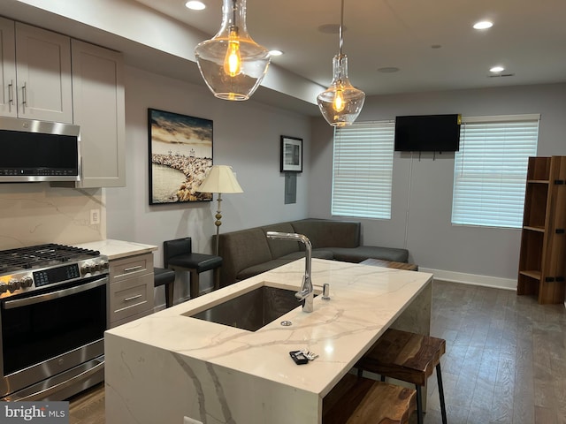 kitchen with light stone countertops, sink, an island with sink, pendant lighting, and appliances with stainless steel finishes