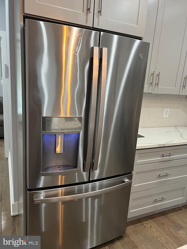 interior details featuring tasteful backsplash, light stone counters, hardwood / wood-style floors, stainless steel fridge with ice dispenser, and gray cabinets