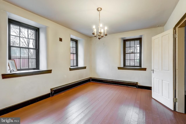 empty room with a chandelier, a baseboard heating unit, and hardwood / wood-style flooring