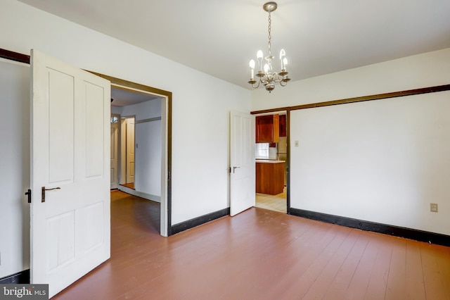 empty room with hardwood / wood-style floors and an inviting chandelier