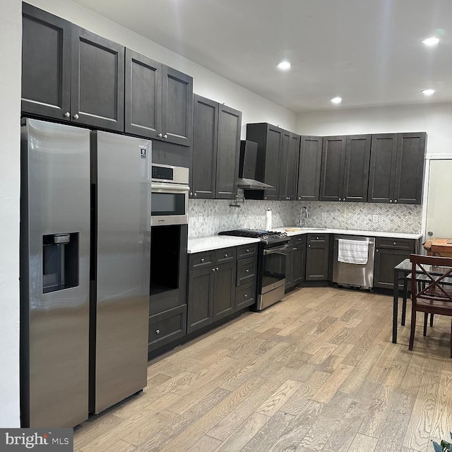 kitchen featuring light hardwood / wood-style floors, wall chimney range hood, sink, and appliances with stainless steel finishes