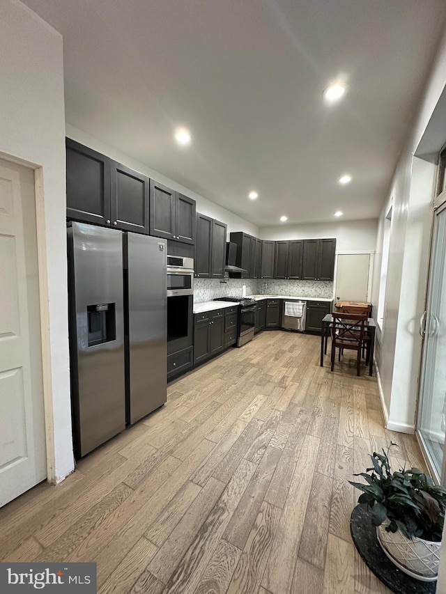 kitchen with tasteful backsplash, light wood-type flooring, stainless steel appliances, and wall chimney range hood