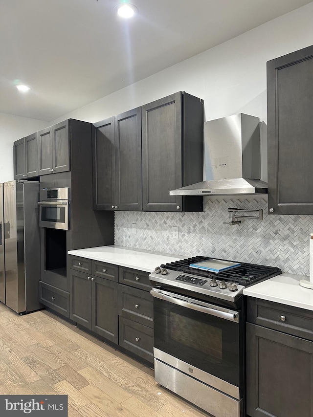 kitchen featuring light hardwood / wood-style floors, wall chimney range hood, stainless steel appliances, and tasteful backsplash