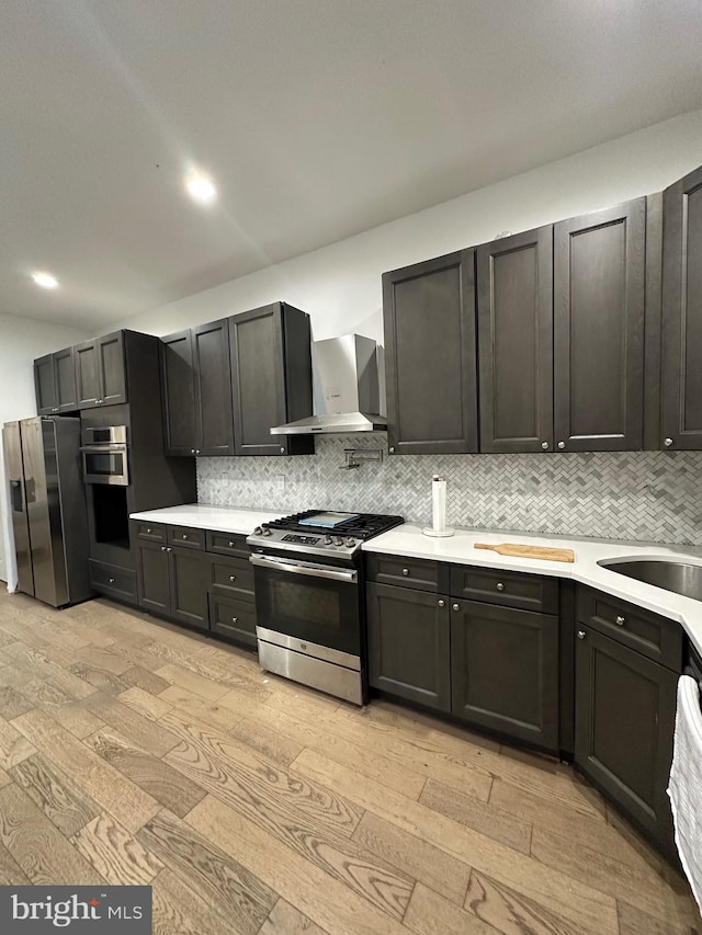 kitchen featuring light hardwood / wood-style floors, wall chimney range hood, appliances with stainless steel finishes, and tasteful backsplash