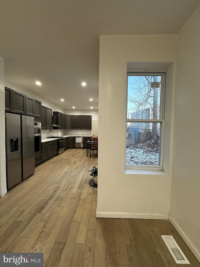 kitchen with wall chimney range hood, light hardwood / wood-style flooring, stainless steel refrigerator with ice dispenser, decorative backsplash, and double wall oven