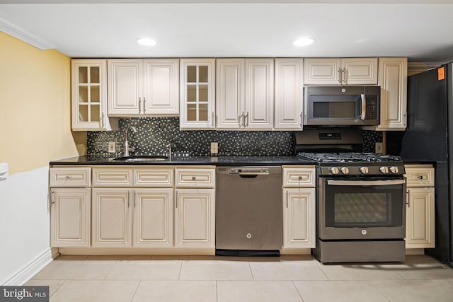 kitchen featuring appliances with stainless steel finishes, ornamental molding, sink, light tile patterned floors, and cream cabinetry