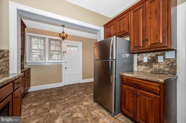 kitchen with decorative backsplash, hanging light fixtures, stainless steel refrigerator, and dark stone counters