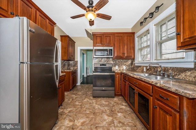 kitchen with appliances with stainless steel finishes, backsplash, dark stone counters, ceiling fan, and sink