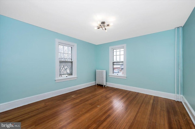 empty room featuring a wealth of natural light, dark hardwood / wood-style floors, an inviting chandelier, and radiator