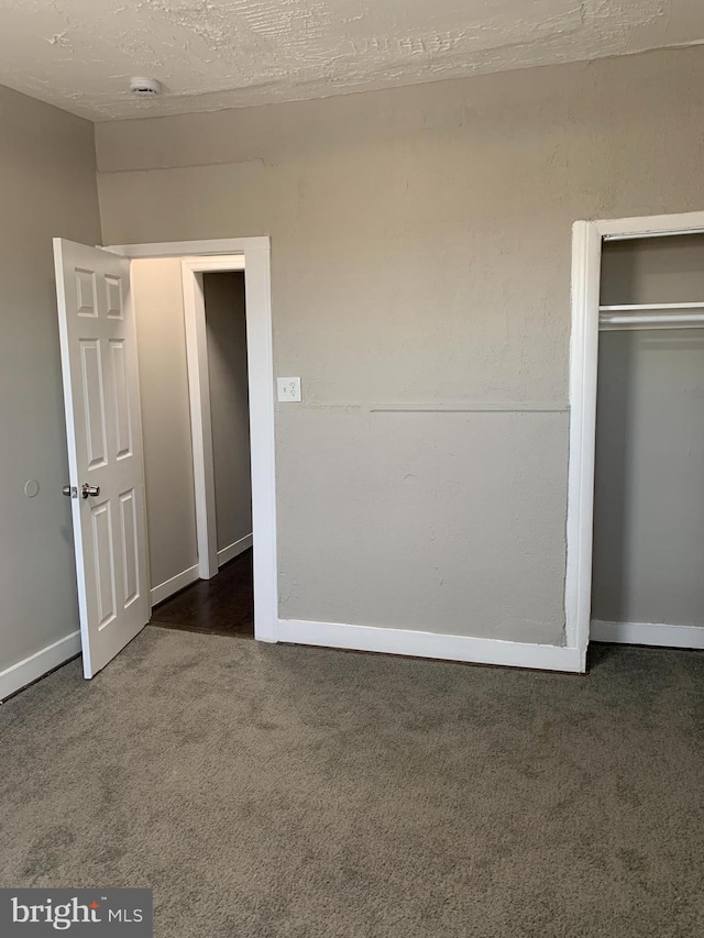 unfurnished bedroom featuring a textured ceiling, dark carpet, and a closet