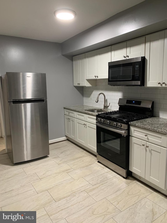 kitchen featuring decorative backsplash, light stone counters, stainless steel appliances, sink, and white cabinets