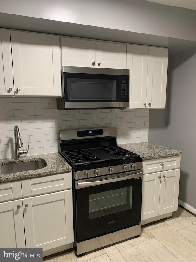 kitchen with sink, tasteful backsplash, stone countertops, white cabinets, and appliances with stainless steel finishes