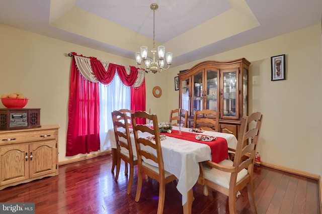 dining room featuring a raised ceiling, dark wood-type flooring, and an inviting chandelier