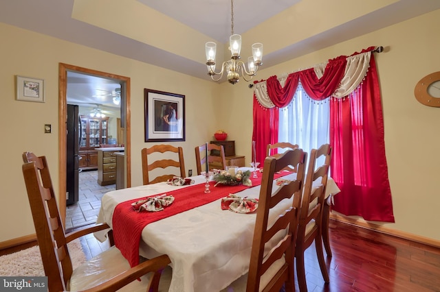 dining space with a tray ceiling, ceiling fan with notable chandelier, and hardwood / wood-style flooring