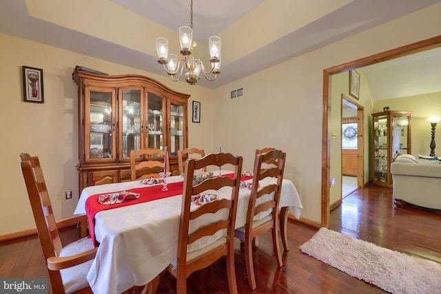 dining space with dark hardwood / wood-style floors, lofted ceiling, and an inviting chandelier