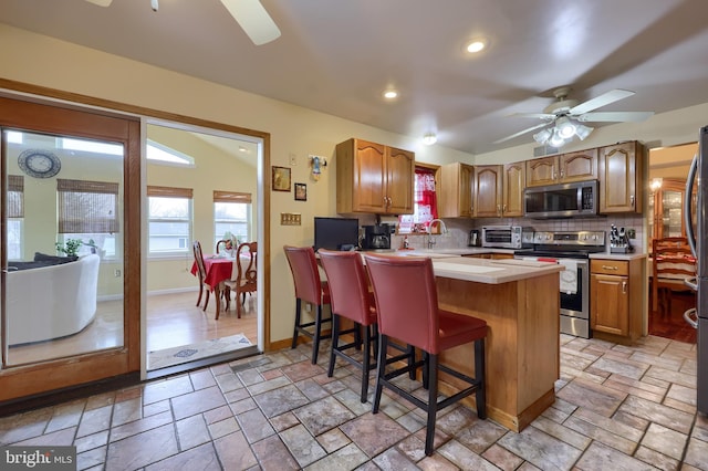 kitchen with backsplash, a kitchen breakfast bar, ceiling fan, appliances with stainless steel finishes, and kitchen peninsula