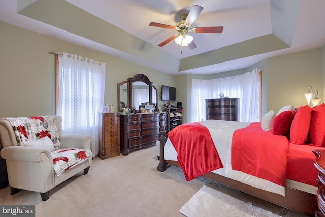 carpeted bedroom featuring a raised ceiling, multiple windows, and ceiling fan