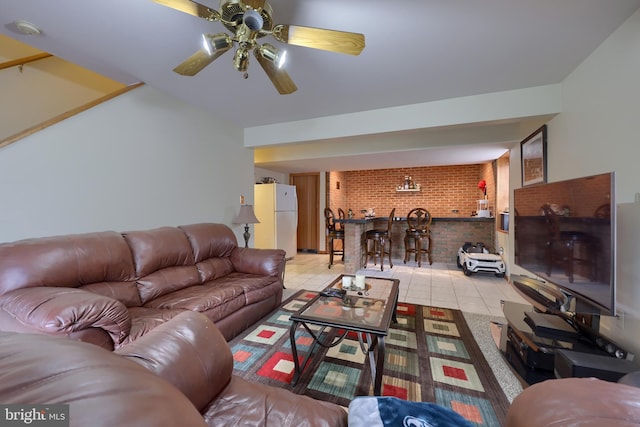 tiled living room featuring ceiling fan, brick wall, and indoor bar