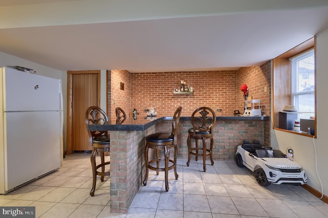 kitchen featuring brick wall, white refrigerator, kitchen peninsula, a breakfast bar, and light tile patterned floors