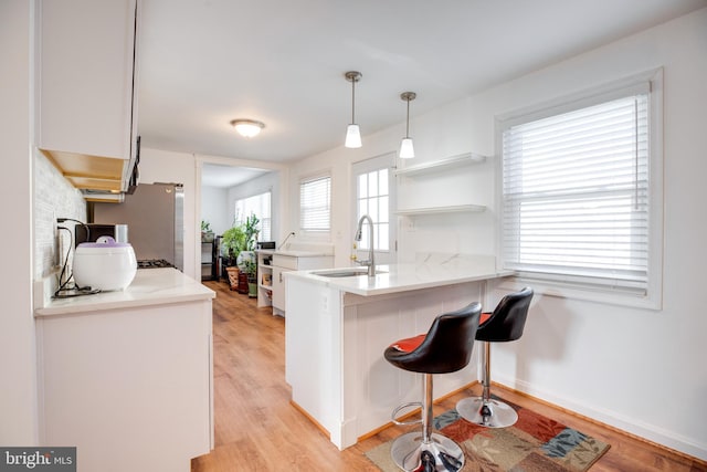 kitchen featuring kitchen peninsula, a breakfast bar, sink, light hardwood / wood-style floors, and white cabinetry