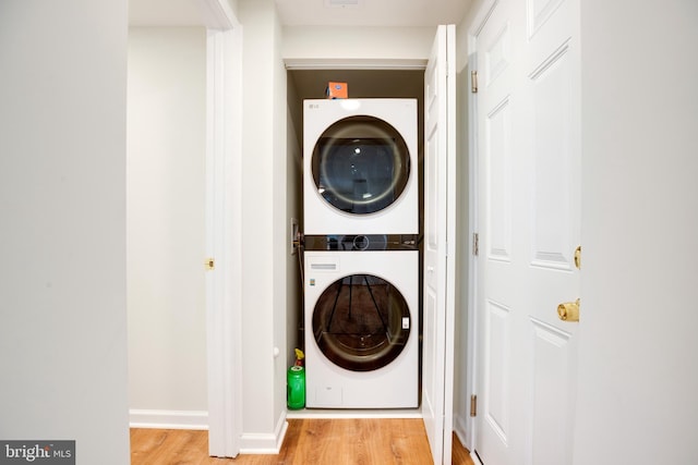 laundry room with light wood-type flooring and stacked washer / drying machine