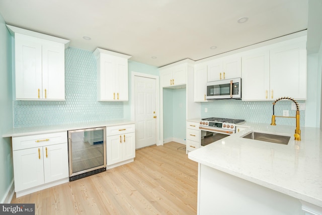 kitchen with light stone countertops, sink, wine cooler, white cabinets, and appliances with stainless steel finishes