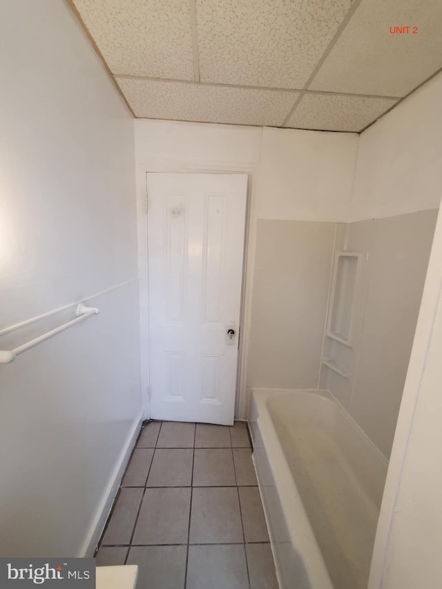 bathroom with tile patterned floors, a paneled ceiling, and a bath