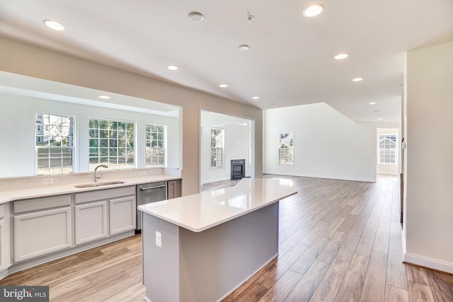 kitchen featuring stainless steel dishwasher, a kitchen island, light hardwood / wood-style floors, and sink