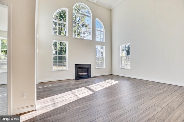 unfurnished living room featuring plenty of natural light, a towering ceiling, ornamental molding, and light wood-type flooring