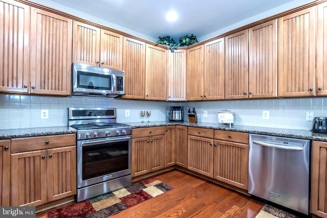 kitchen with backsplash, dark stone countertops, dark hardwood / wood-style floors, and appliances with stainless steel finishes